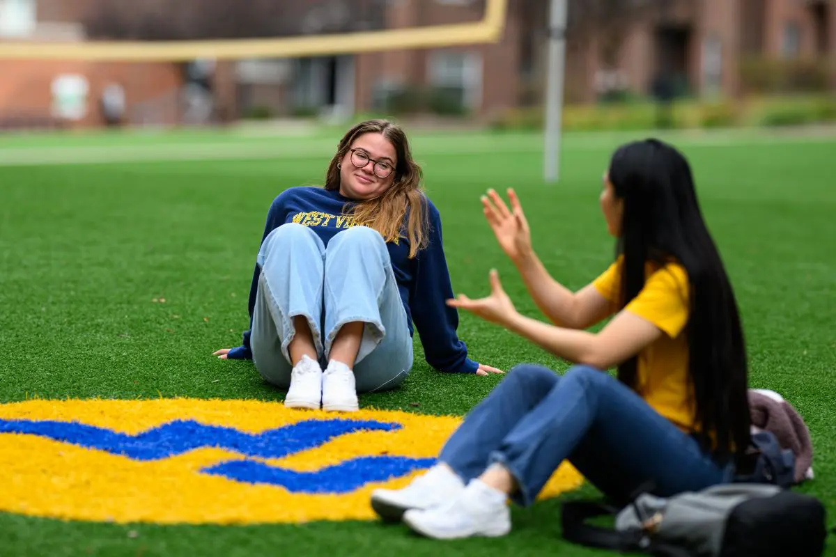 Students talking while sitting on the WVU football field