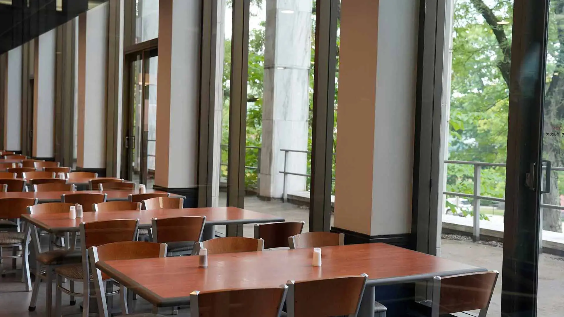 Empty tables and chairs along large windows in dining hall
