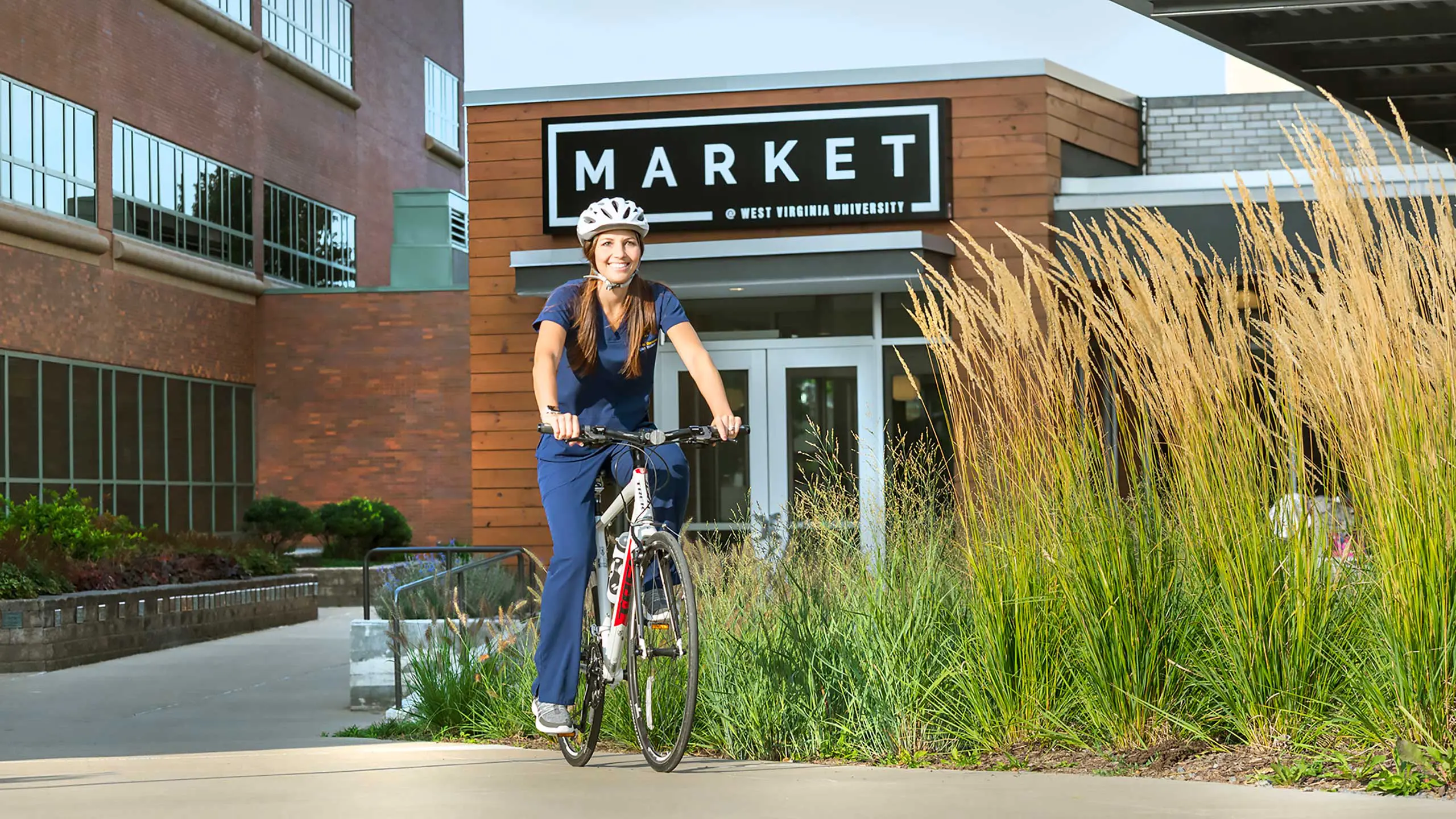 A student wearing blue scrubs and a bicycle helmet, riding a bike past a sign that reads "Market"