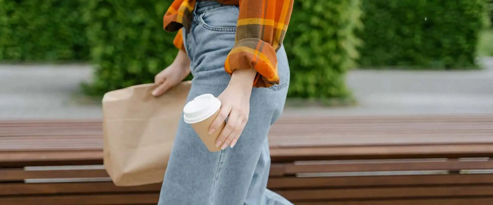 Person walking holding brown paper bag and paper coffee cup