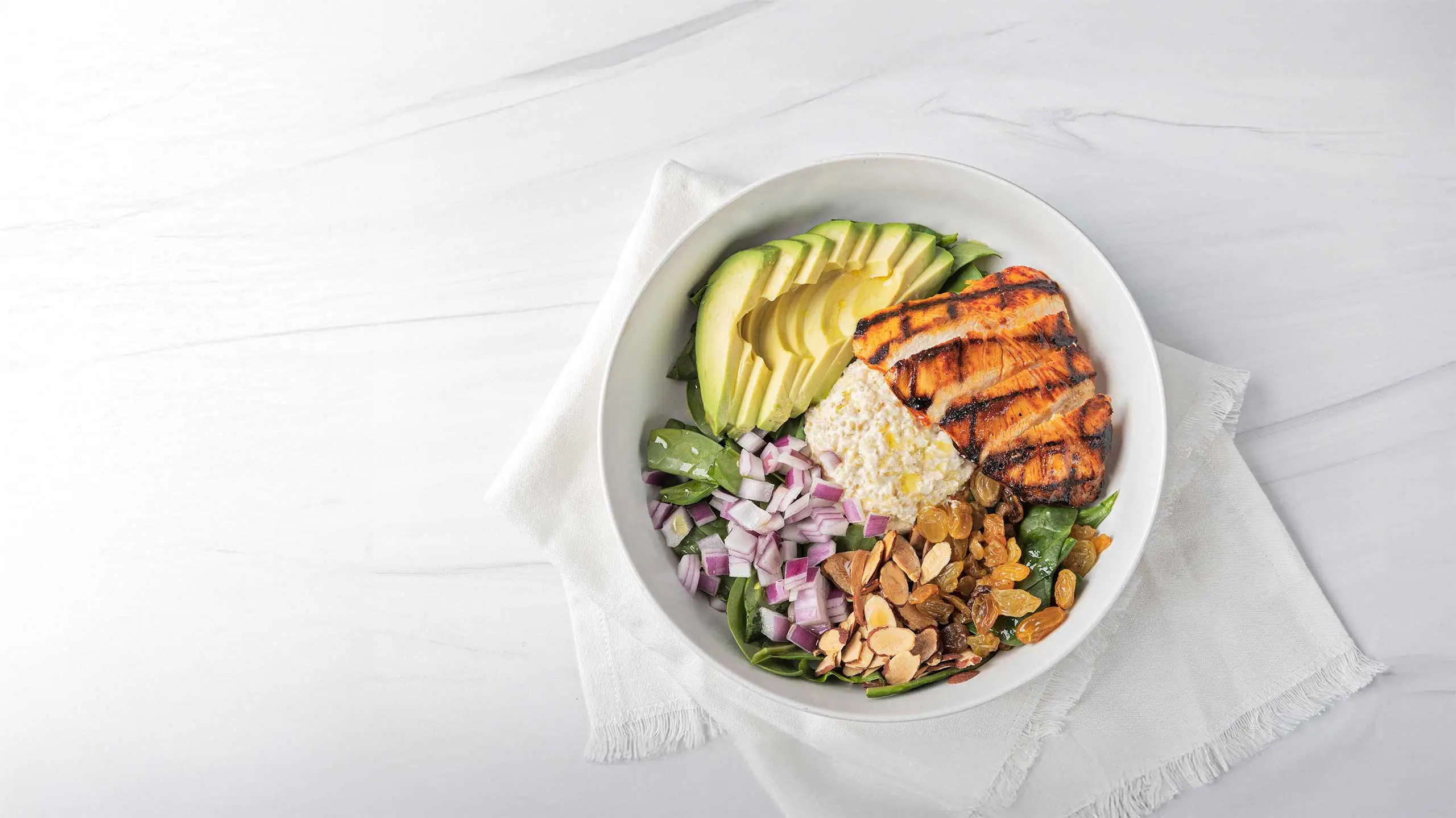 Bowl of salad with grilled chicken, avocado, almonds, red onion and feta cheese