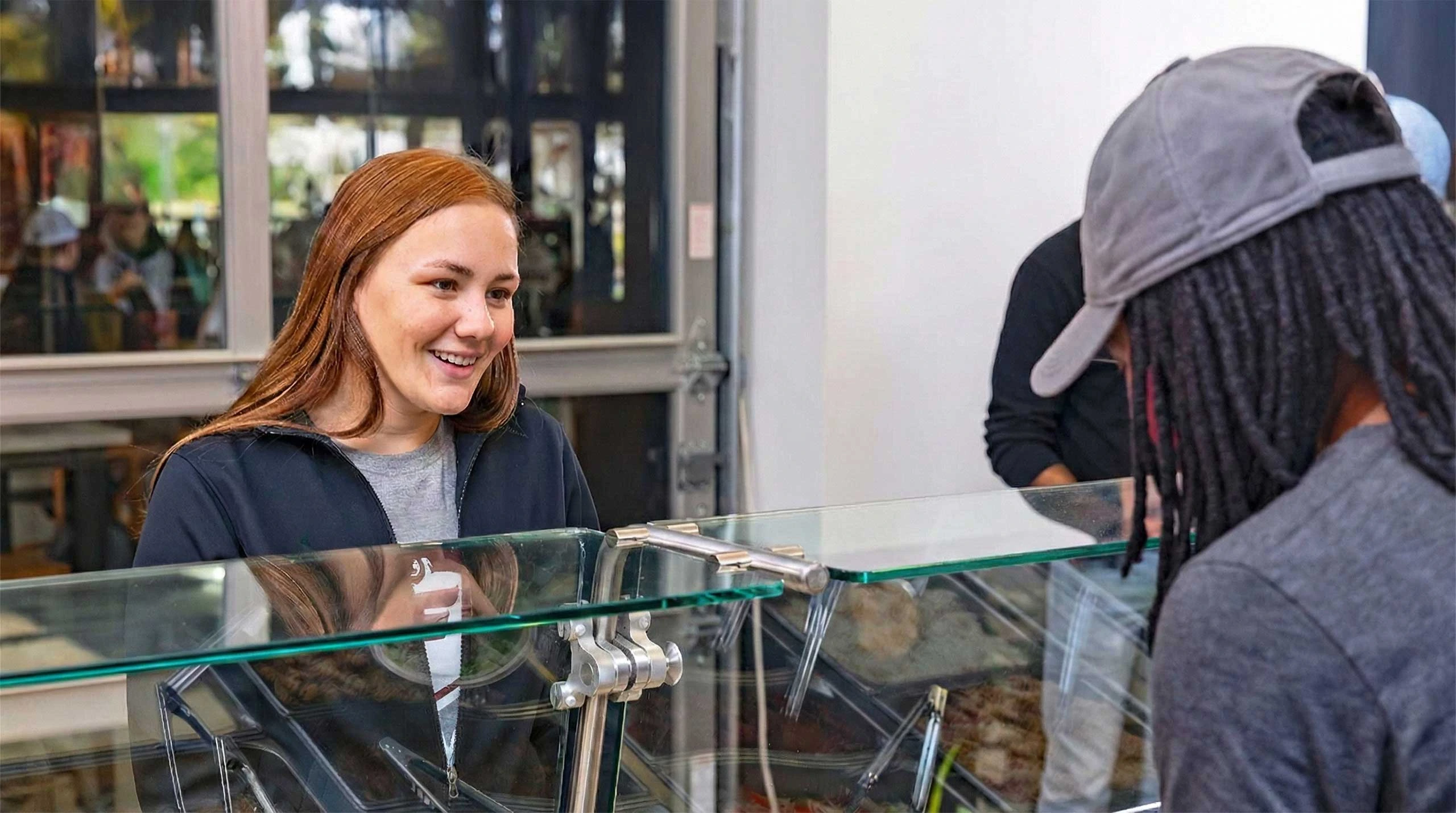 Student smiling while watching employee prepare meal