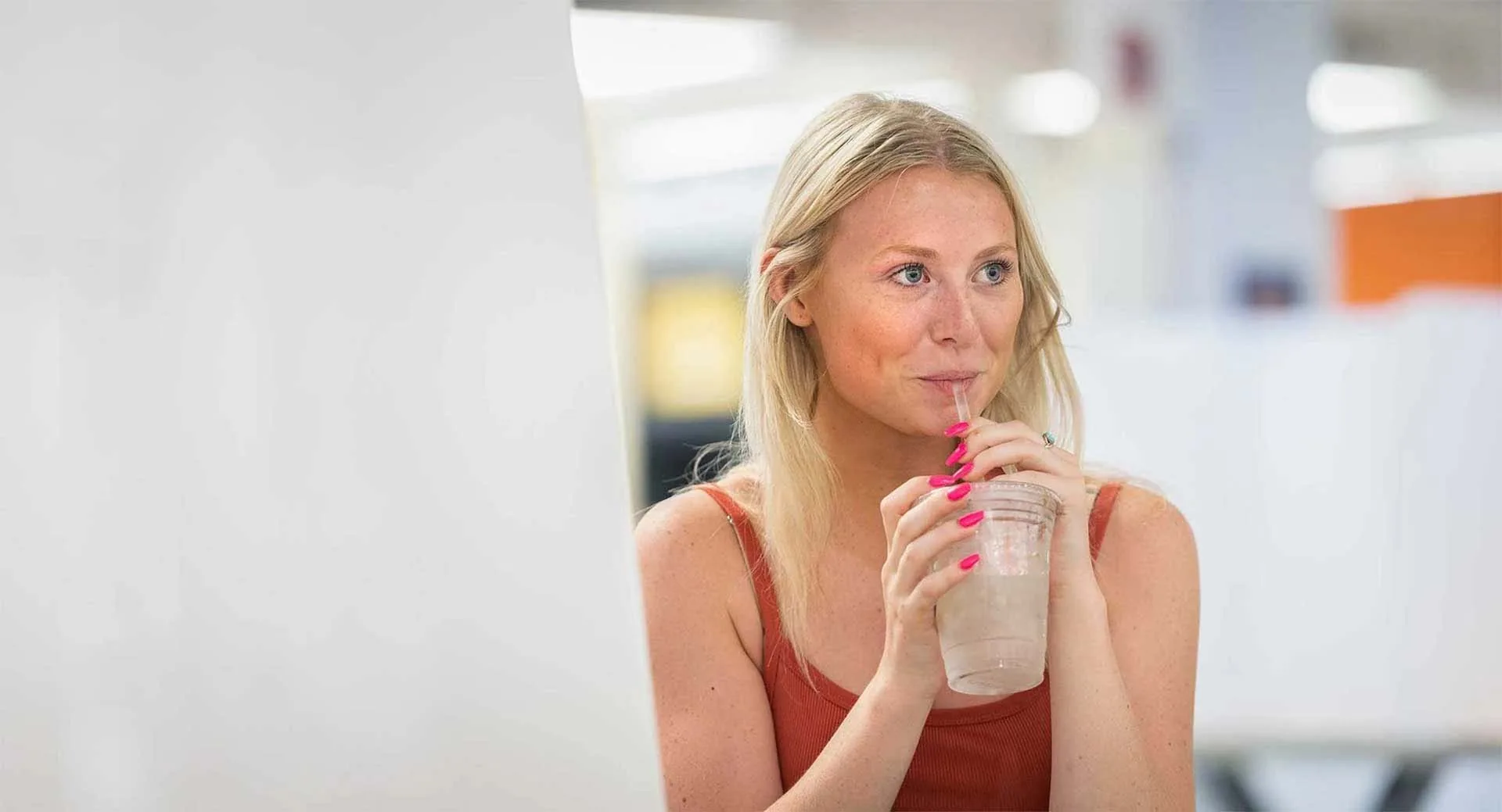 Student sipping iced beverage with WVU dining hall in background